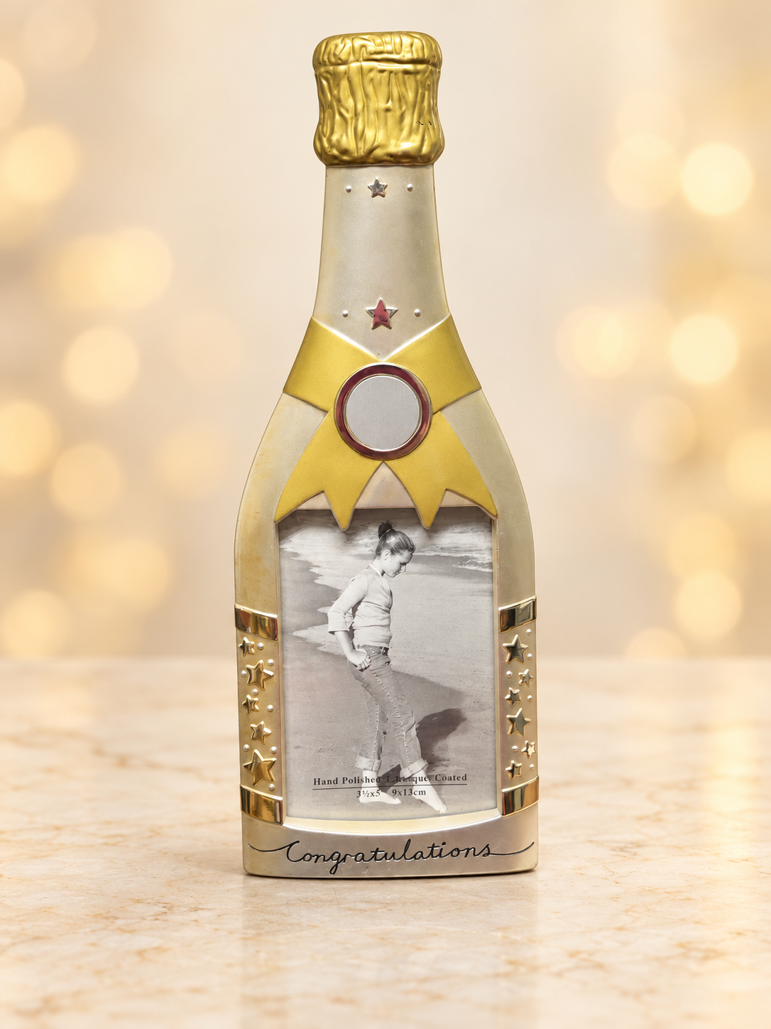 Gold- and silver-tone champagne bottle Congratulations picture frame for a 3.5 × 5-inch photo, on a cream background